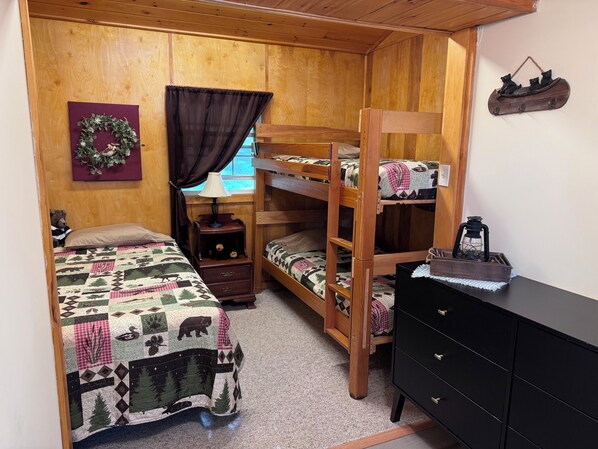 A cozy room with two bunk beds, a wooden dresser, a nightstand, a lamp, and a decorative wreath on the wall. - Cozy Messalonskee Lake Cabin – Dock, Kayaks & Family‑Friendly, Sleeps 5 (Sidney)