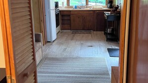 A compact kitchen with wooden cabinets, a refrigerator, a sink, and a window. - Cozy Messalonskee Lake Cabin – Dock, Kayaks & Family‑Friendly, Sleeps 5 (Sidney)