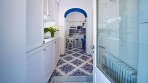 A narrow hallway with a patterned floor leading to a kitchen area with white cabinets and a blue archway. - AMORE RENTALS - Maison Don Rafe’ con Vista Mare e Solarium (Campania)