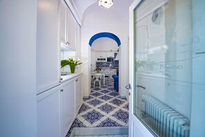A narrow hallway with a patterned floor leading to a kitchen area with white cabinets and a blue archway.
