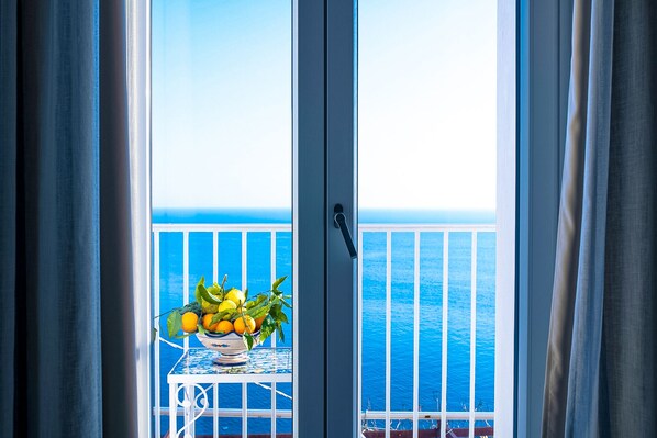 A balcony with a table holding a bowl of fruit, overlooking a body of water.