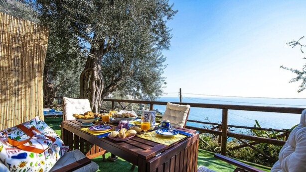An outdoor dining area with a table set for breakfast, overlooking a scenic view. - AMORE RENTALS - Maison Don Rafe’ con Vista Mare e Solarium (Campania)