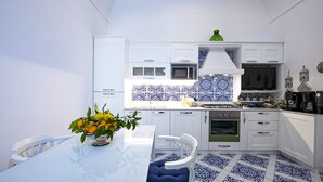 A modern kitchen with white cabinetry, a blue and white patterned backsplash, and a dining area with a white table and chairs. - AMORE RENTALS - Maison Don Rafe’ con Vista Mare e Solarium (Campania)