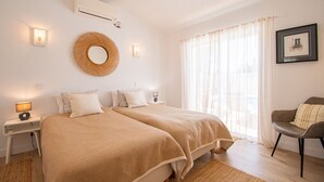 Une chambre avec deux lits, un miroir rond, un climatiseur fixé au mur et une fenêtre avec des rideaux légers.