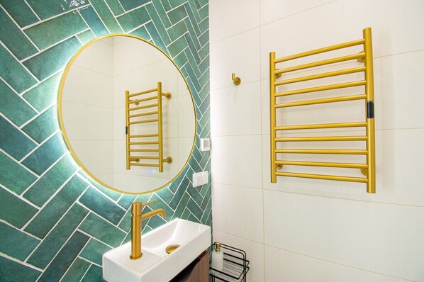 Een badkamer met een wit wastafel, gouden accessoires, een spiegel en een handdoekhouder.