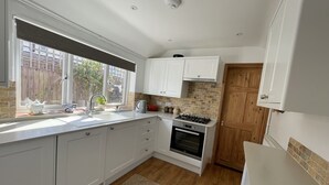 Eine moderne Küche mit weißen Schränken, einem Backofen, einem Gasherd und einem Fenster mit Blick auf einen Holzzaun und Grünflächen.