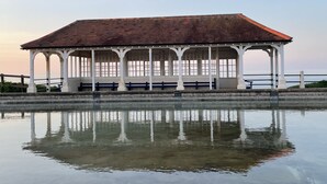 Ein Pavillon mit Ziegeldach und weißen Säulen, gelegen am Ufer eines stillen Gewässers.