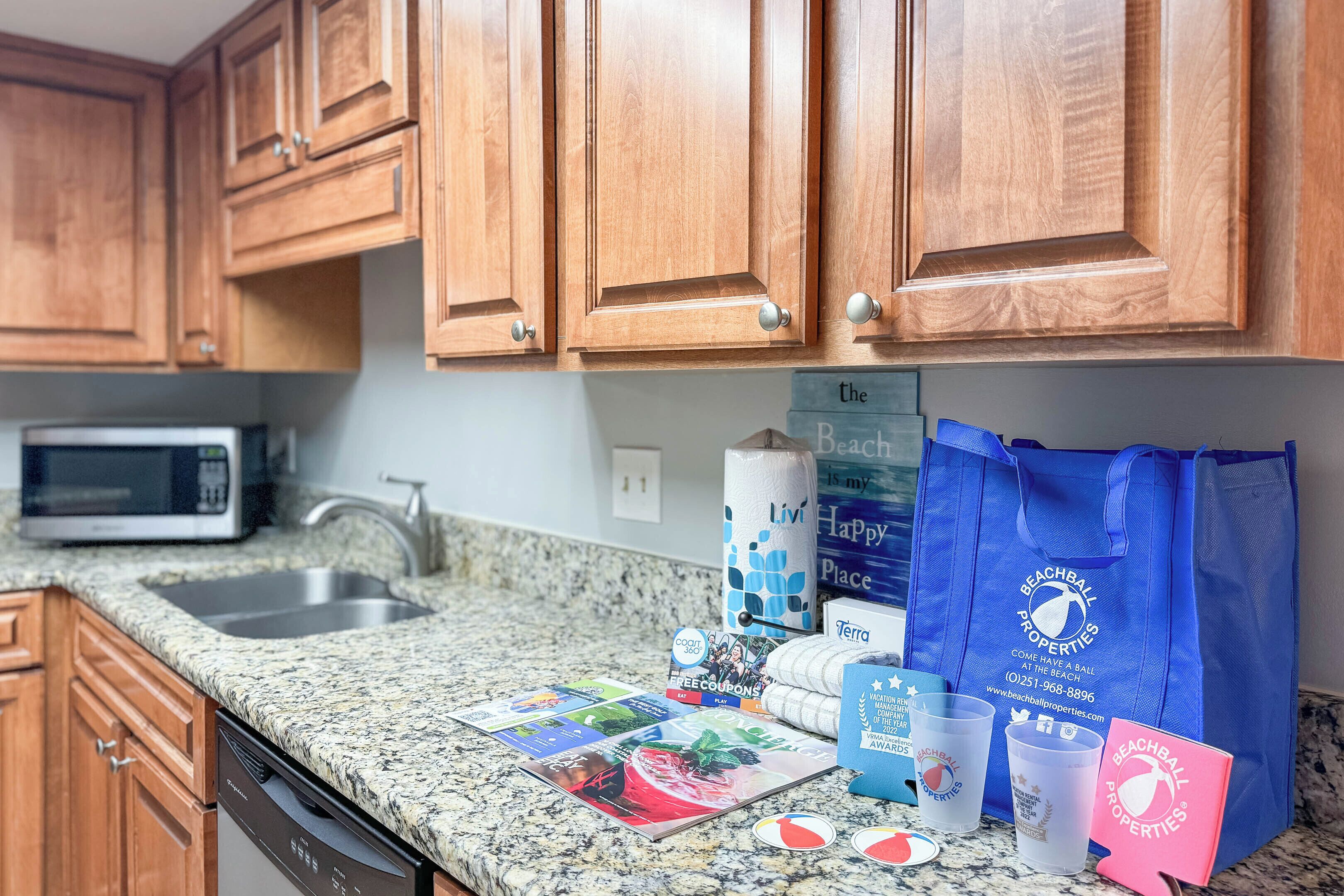 A kitchen with wooden cabinets, a granite countertop, a microwave, and a dishwashing area.