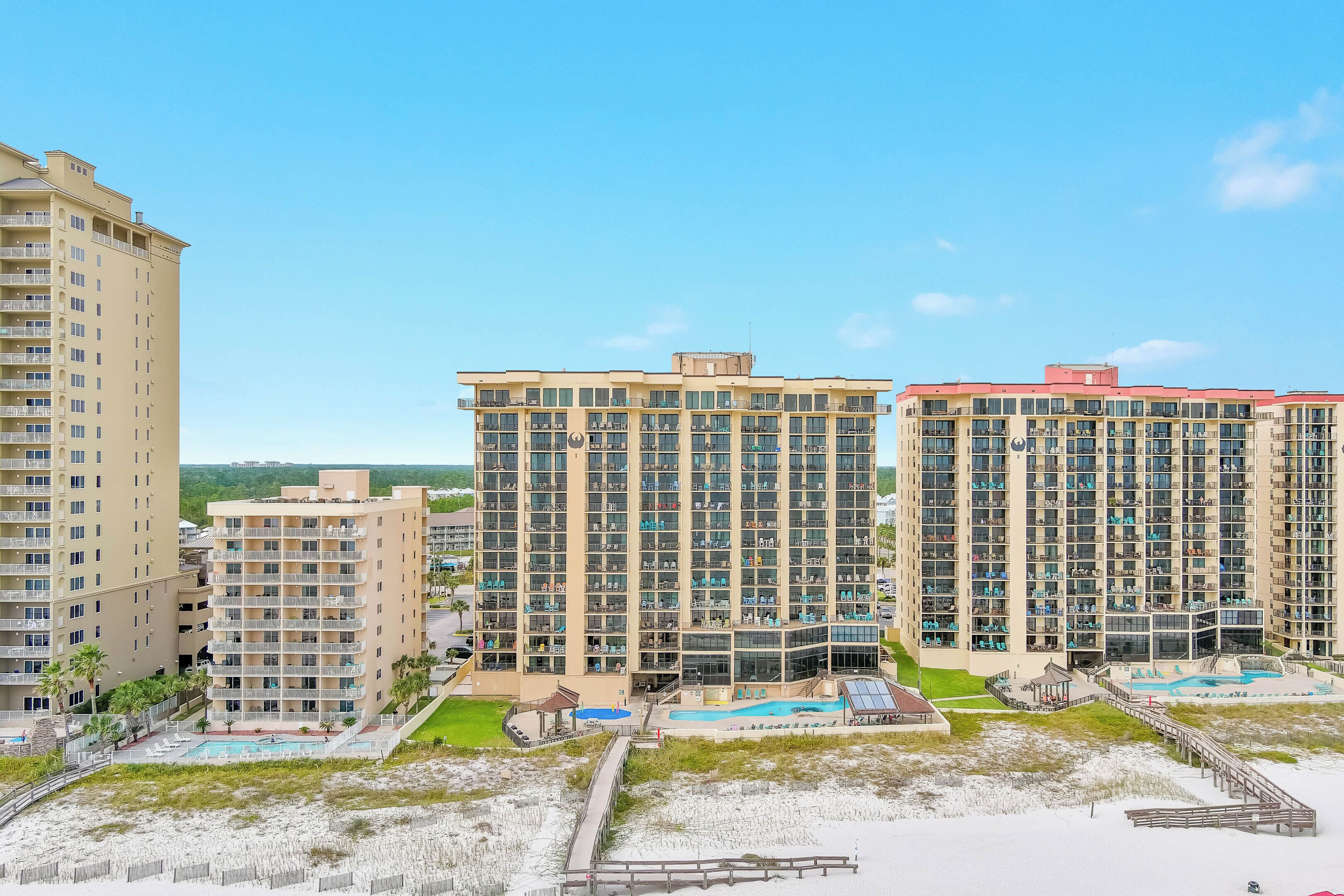 A high-rise hotel with multiple balconies, a swimming pool, and a beach area.
