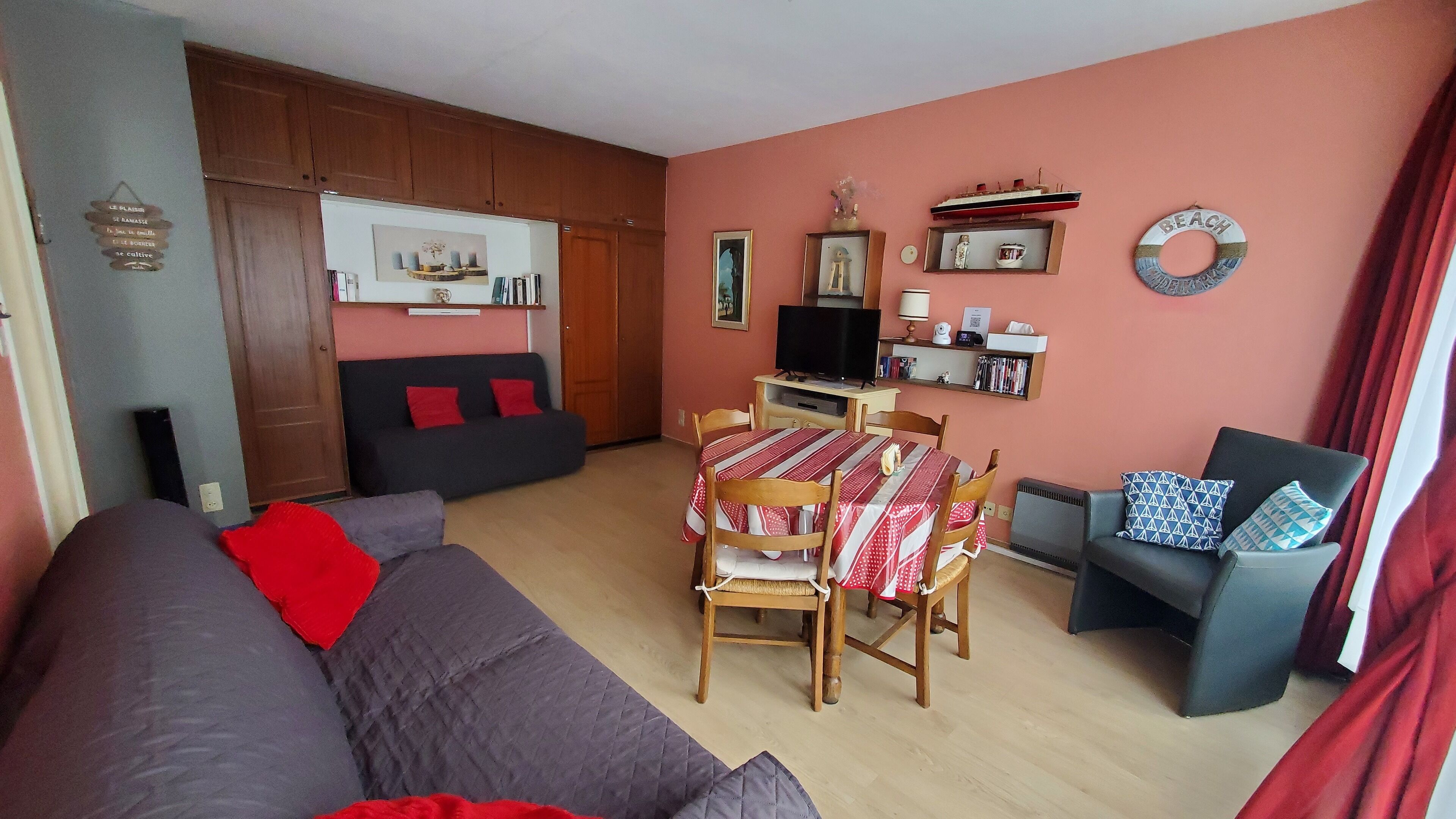 A cozy living room with a sofa, a dining table with chairs, a TV, and a bookshelf.