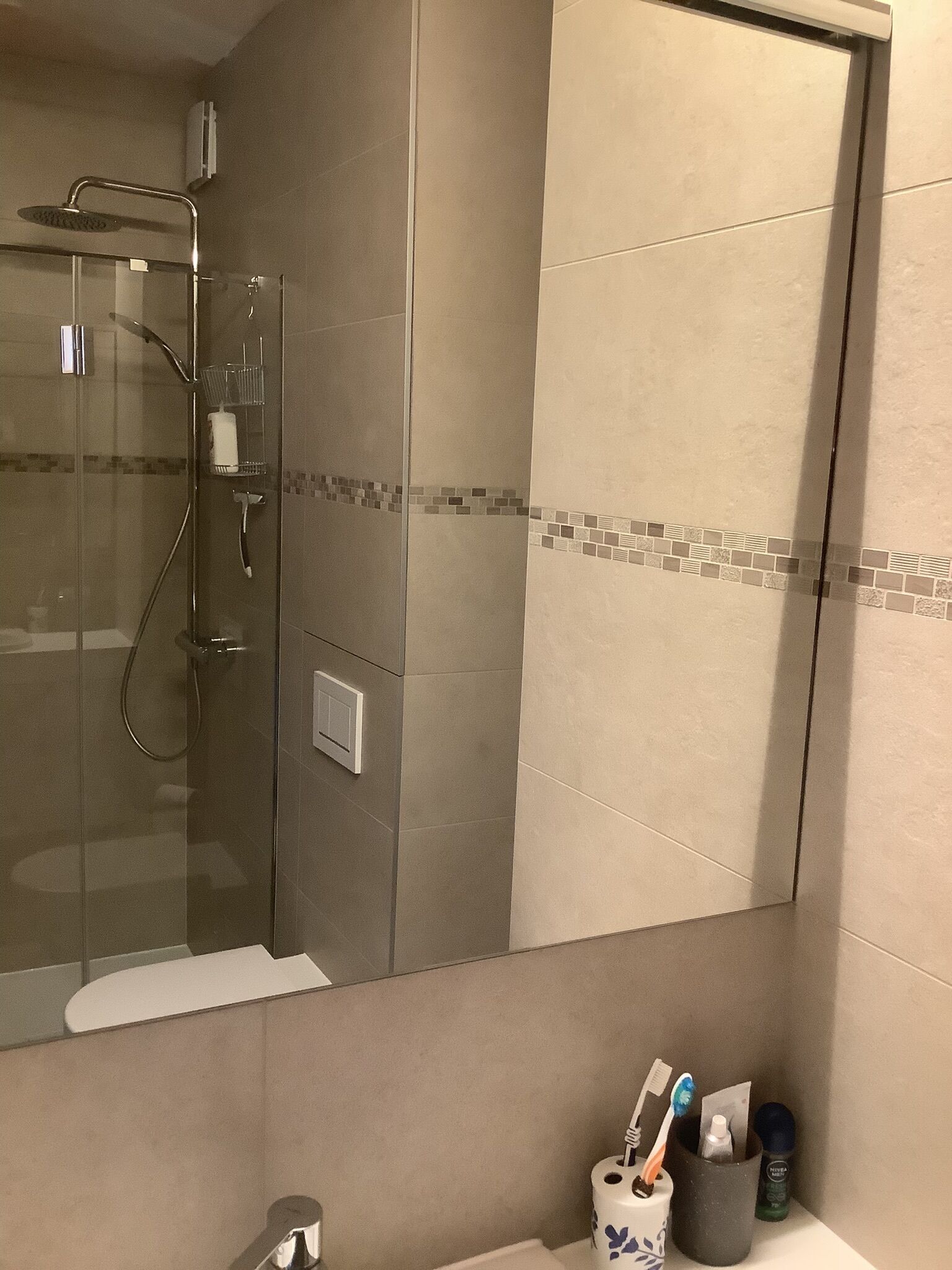 Une salle de bain moderne avec une douche à parois de verre, un lavabo blanc et un miroir.