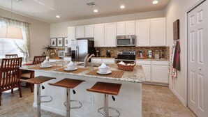 Una cocina moderna con armarios blancos, encimera de granito, electrodomésticos de acero inoxidable y una isla central con taburetes de bar.
