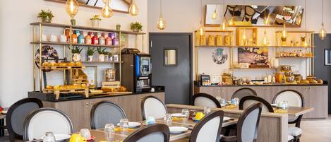 Un restaurant doté de plusieurs tables et chaises, d’étagères remplies de produits alimentaires et de luminaires suspendus.