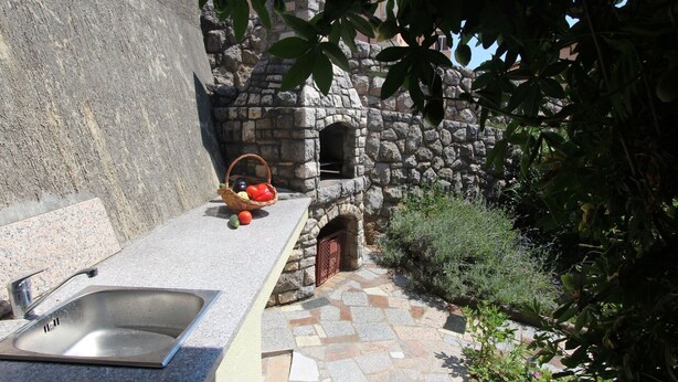 Un forno in pietra, un lavello e un cesto pieno di frutta, in un ambiente esterno rustico.