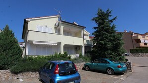 Un edificio a due piani con un balcone, auto parcheggiate e un grande albero sempreverde.