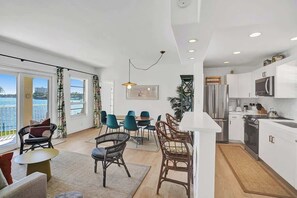 A modern kitchen with white cabinets, a stainless steel refrigerator, and a dining area with blue chairs.
