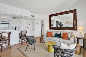 A modern living room with wicker furniture, a sofa with colorful cushions, and a large mirror on the wall.