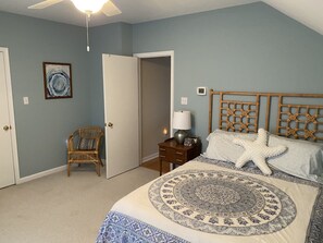 Een slaapkamer met een bed, een stoel, een nachtkastje, een lamp en een plafondventilator.