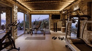 A gym with exercise equipment, a treadmill, and a view of the outdoors. - Villa Amira NEW Luxury Property in Ftelia with Amazing Sea views & Heated pool (Mikonos)
