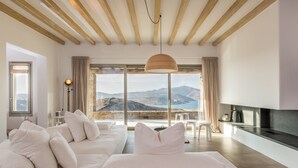 A modern bedroom with a large window offering a mountain view, a sofa, and a TV. - Villa Amira NEW Luxury Property in Ftelia with Amazing Sea views & Heated pool (Mikonos)