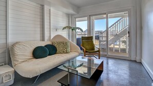Ein Wohnzimmer mit einer Couch, einem Glastisch, einem grünen Sessel und Blick auf eine nach draußen führende Treppe.