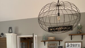 A kitchen with a wooden table, chairs, a hanging light fixture, and a coffee-themed decor.