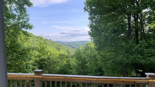 A wooden deck with a railing and a view of a forested valley.