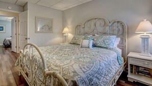 Een keurig opgemaakt slaapkamer met een metalen bed, beddengoed met een patroon, bedlampen en een boekenplank.