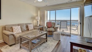 Een woonkamer met een bank, salontafel en fauteuil, een balkon met uitzicht, en een plafondventilator.
