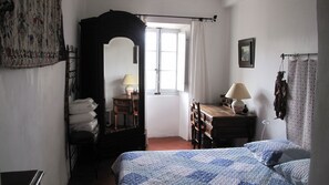 Ein Schlafzimmer mit Bett, Kommode, Spiegel, einem Fenster mit Vorhängen und einer Lampe.
