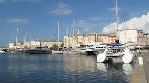 A marina with several sailboats docked, a waterfront promenade, and buildings with balconies in the background.