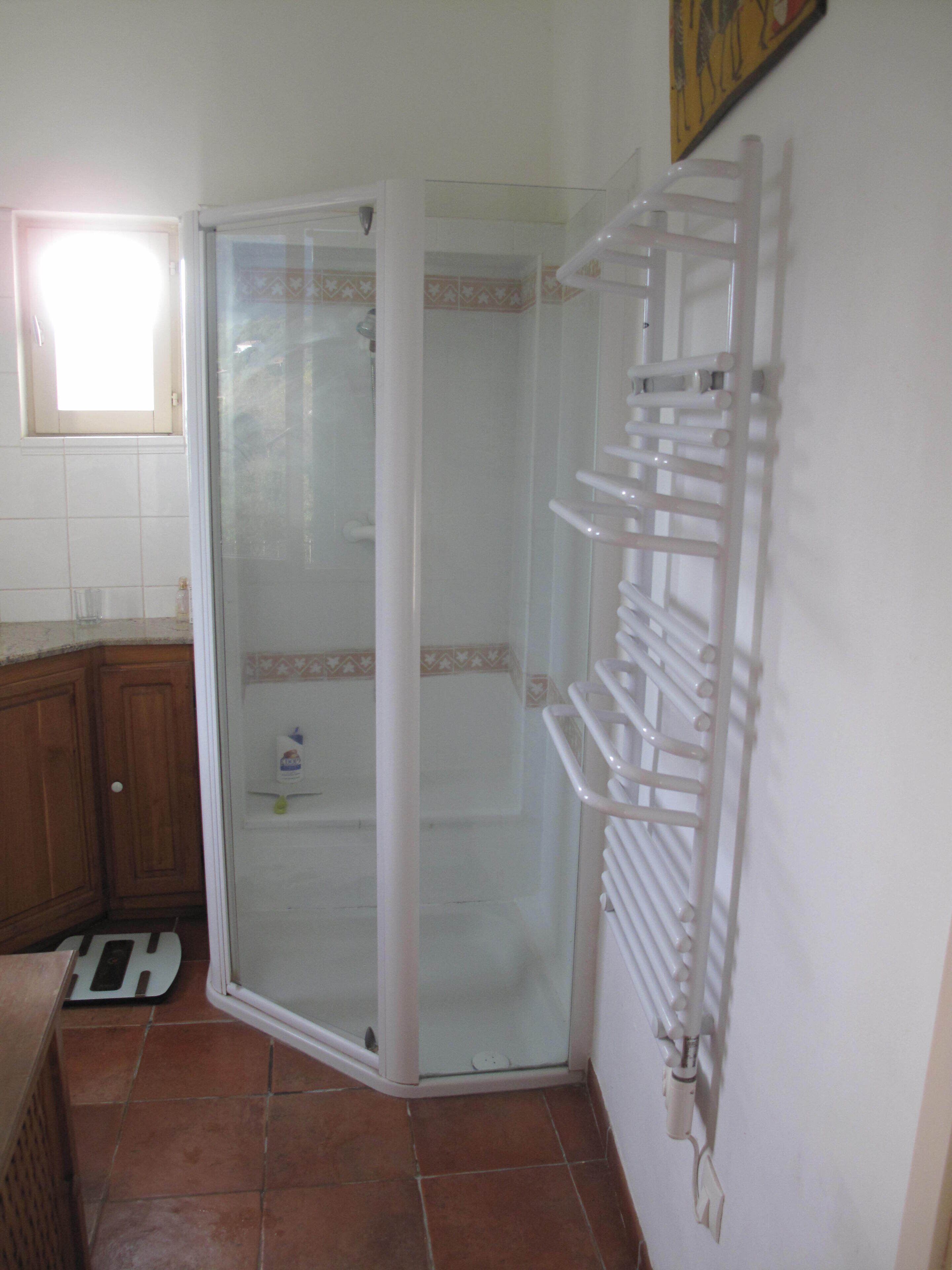 Un baño con cabina de ducha de vidrio, un perchero blanco y suelo de baldosas.