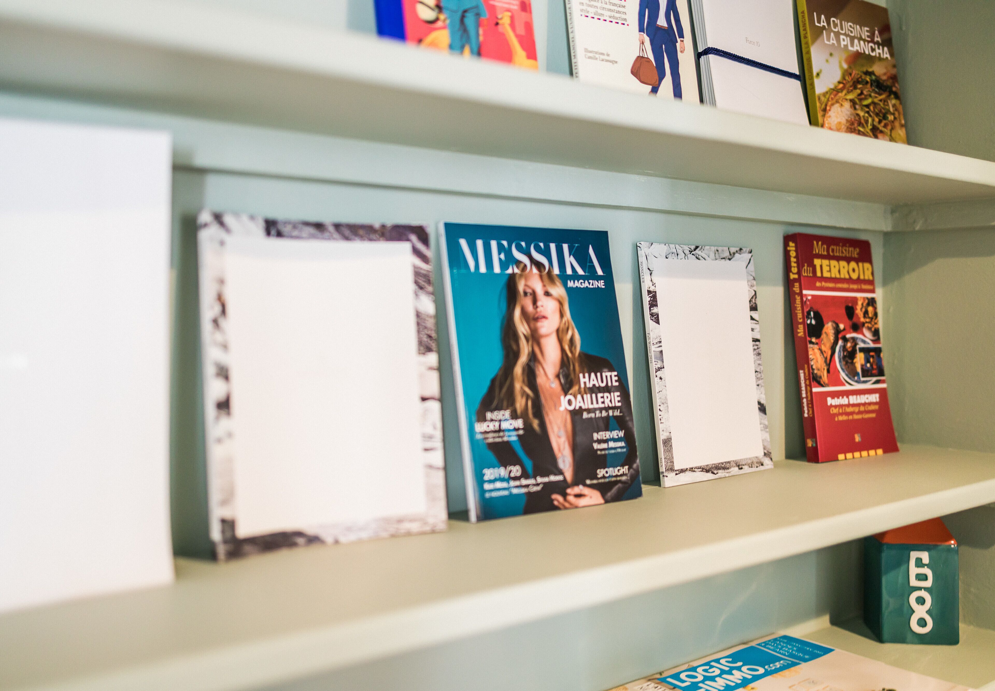 A shelf with various magazines and books, including 'Messika Magazine' and 'La Cuisine à la Plancha'.