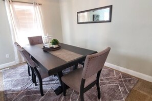 Un coin repas avec une table en bois foncé, quatre chaises, une petite plante en pot et un miroir au mur.