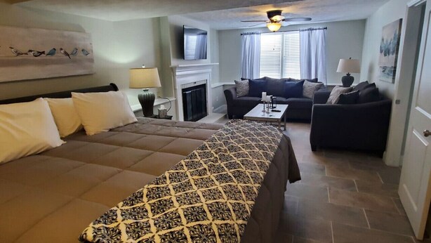 Ein Hotelzimmer mit einem großen Bett, einer Couch, einem kleinen Tisch, einem Kamin und einem Deckenventilator.