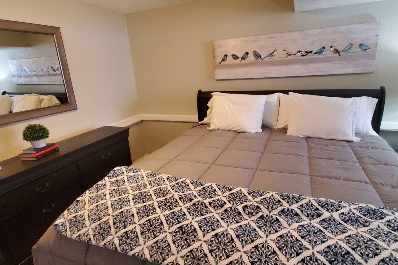 A bedroom with a bed, a dresser, a mirror, and a wall art piece.