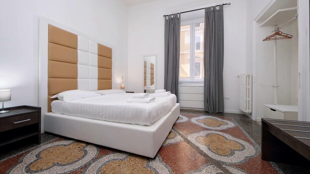 A modern bedroom with a large bed, a bedside table, a wardrobe, and a window with curtains. - Flatinrome Termini 2 (ROMA)