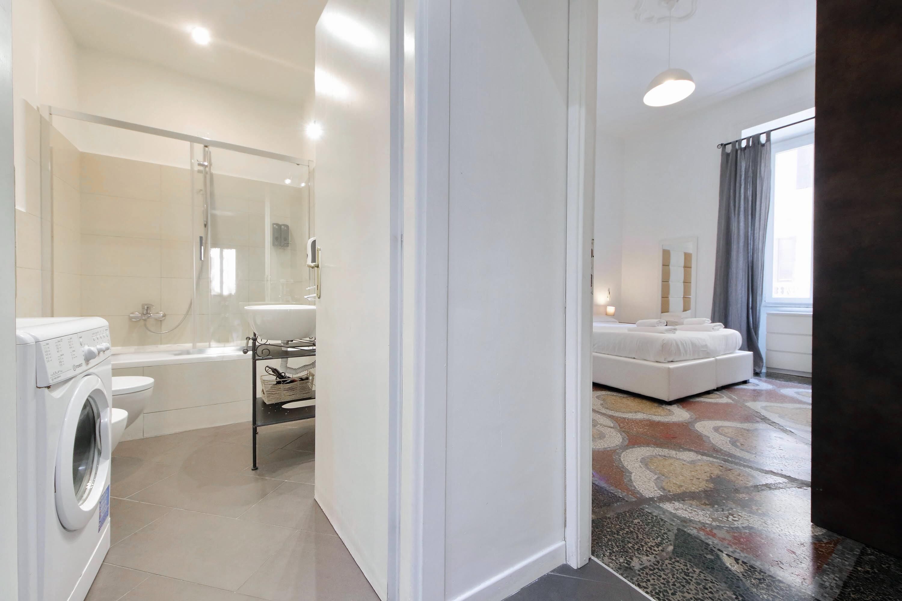 A modern bathroom with a washing machine, a glass shower enclosure, and a white sink.