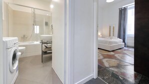 A modern bathroom with a washing machine, a glass shower enclosure, and a white sink. - Flatinrome Termini 2 (ROMA)