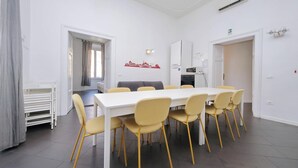 A dining area with a white table and yellow chairs, a grey sofa, and a wall with a red cityscape mural. - Flatinrome Termini 2 (ROMA)