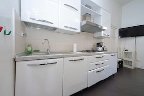 A modern kitchen with white cabinetry, a stainless steel sink, and a gas stove. - Flatinrome Termini 2 (ROMA)