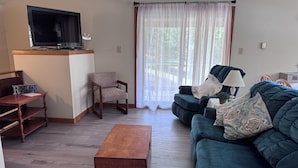 Un salon avec un téléviseur, une table en bois, un canapé et un fauteuil.