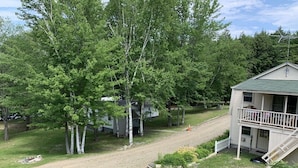 Une cabane à deux étages avec un balcon, entourée d’arbres et bordée d’un sentier de terre.