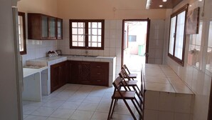 A kitchen with white tiles, wooden cabinets, a sink, and a dining area with chairs. - Sparkle Guesthouse - Self-Catering with private pool and garden (Maputo)