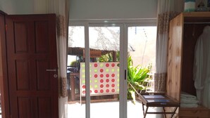 A room with a wooden door, a sliding glass door leading to an outdoor area with a thatched roof, a table with a white cloth, and a wooden cabinet. - Sparkle Guesthouse - Self-Catering with private pool and garden (Maputo)