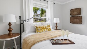 Habitación de hotel ordenada con cama, dos mesitas de noche con lámparas, ventana con cortinas y dos cestos fijados a la pared.
