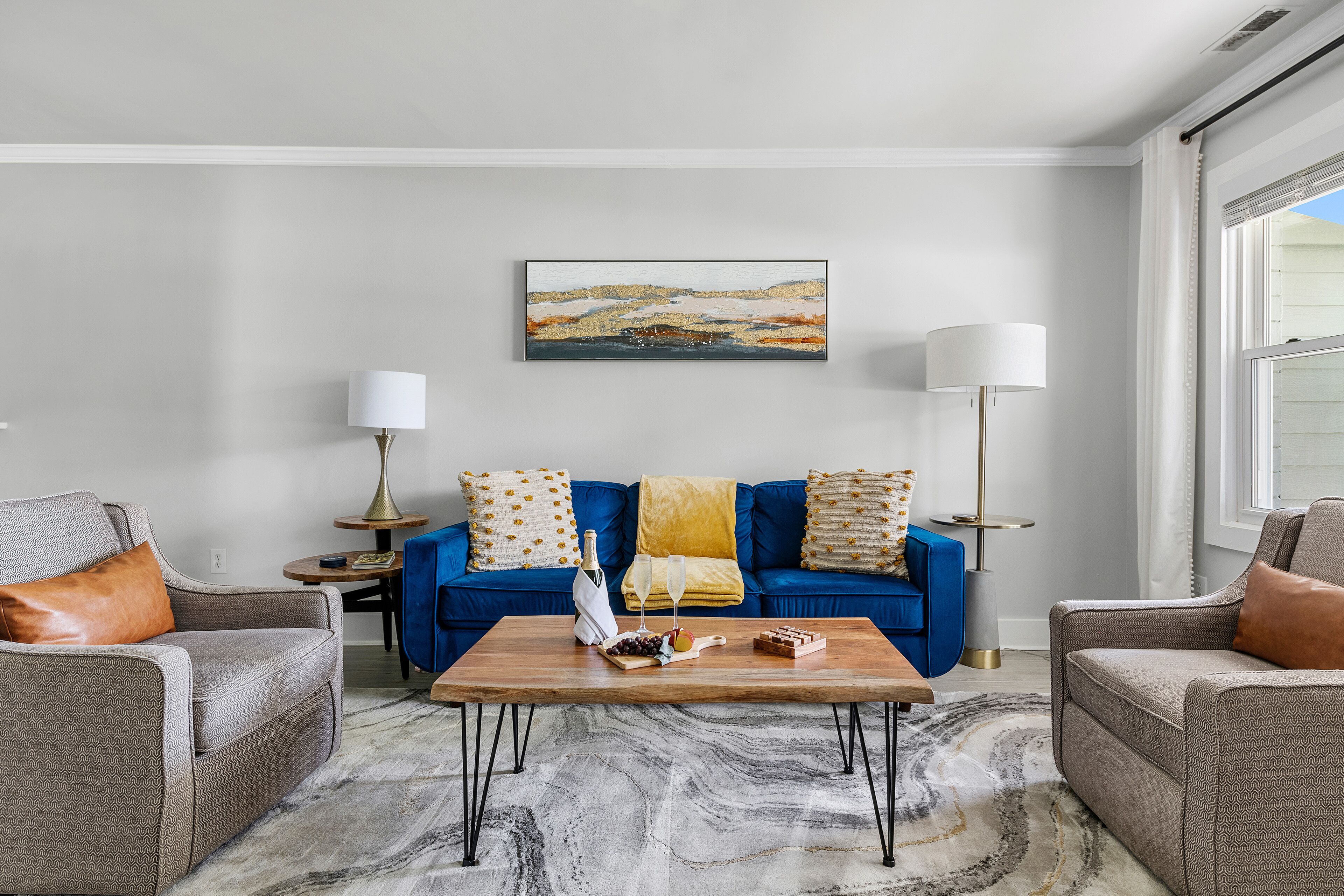 Ein Wohnzimmer mit einem blauen Sofa, zwei Sesseln, einem Couchtisch aus Holz und einem Gemälde an der Wand.