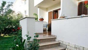 En toetages bygning med hvide facader, en balkon med plantekasser og et lille haveareal med forskellige planter og blomster.