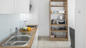 Une cuisine moderne dotée d’un évier en acier inoxydable, d’un plan de travail en bois et d’une étagère intégrée en bois contenant des appareils de cuisine et des ustensiles.