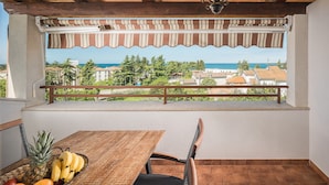 A balcony with a table and chairs, a view of the sea, and buildings in the background. - New and modern stylish apartment with 3 bedrooms in one of the best locations in Porec, close to the beach and with sea view (Porec)